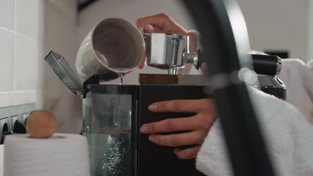 Woman fills coffee machine tank with water closeup. Lady pours water from cup into maker tank for preparing energy drink. Maintenance modern device