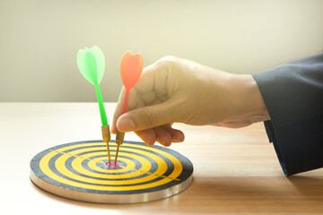 Businessman pointing red dart at center of target board; setting objective or target of investment