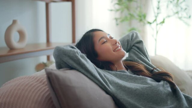 Relaxed young asian woman falling on comfortable sofa at home, female enjoying carefree peaceful weekend relaxation time alone in living room.