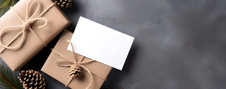 Christmas Presents, Gift Boxes Wrapped With Brown Crafted Paper, Pine Cones And Twig Decor, On Gray Table Background. Empty Paper Card Mockup In Hand. Gift Tag, Business Card Or Invitation Template 