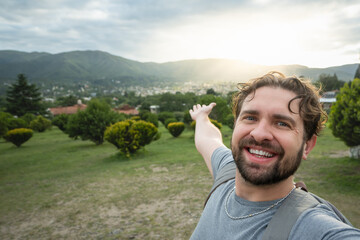 Young hiker taking a selfie portrait at the top of a viewpoint. Happy guy smiling at the camera. Hiking, sport, travel and technology concept. Bright filter. - obrazy, fototapety, plakaty