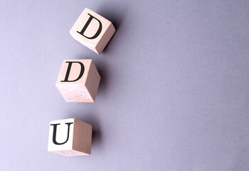 Word DDU on wooden block on the grey background