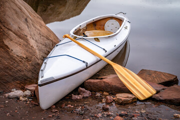 decked expedition canoe with a wooden paddle on a rocky shore of Horsetooth Reservoir near Fort Collins, Colorado, low water level fall or winter scenery - obrazy, fototapety, plakaty