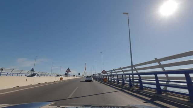 First person view, FPV, from dashcam of car driving across the Constitution of 1812 Bridge, La Pepa, in C&aacute;diz, Andalusia, Spain, Europe. Road trip video in POV, with bright, sunny, clear blue sky