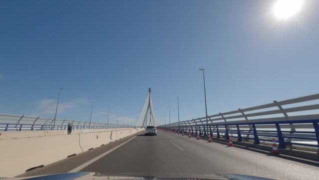 First person view, FPV, from dashcam of car driving across the Constitution of 1812 Bridge, La Pepa, in C&aacute;diz, Andalusia, Spain, Europe. Road trip video in POV, with bright, sunny, clear blue sky