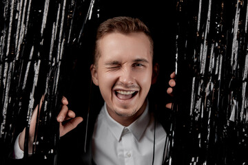 handsome man in black suit winking looking at the camera with happy expression on glitter...