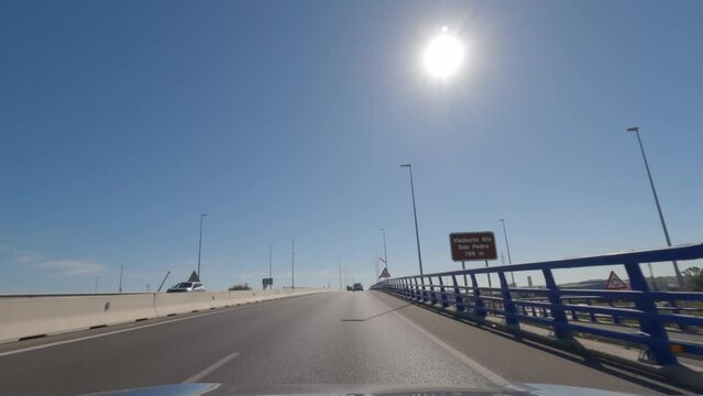 First person view, FPV, from dashcam of car driving across the Constitution of 1812 Bridge, La Pepa, in C&aacute;diz, Andalusia, Spain, Europe. Road trip video in POV, with bright, sunny, clear blue sky