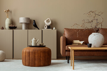 Warm and cozy living room interior with brown sofa, wooden coffee table, round pouf, vase with branch, beige sideboard, pitcher, cup, books and personal accessories. Home decor. Template. - obrazy, fototapety, plakaty