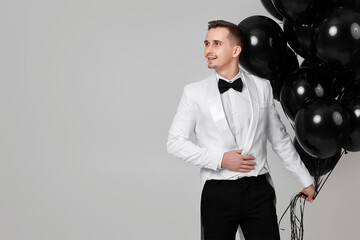 elegant caucasian man in white suit tuxedo with bunch of black air balloons. copy space
