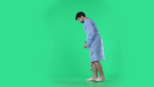 Man in robe making few successful steps with crutch, slowly walking and limping after trauma. Isolated on chroma key green screen.
