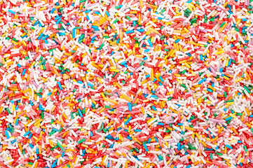 Fototapeta na wymiar Rainbow sprinkles, background and surface. Rod-shaped colorful sugar sprinkles. Tiny candies in a variety of colors, used as sweet decoration and topping for cookies, cakes and ice cream. Food photo.
