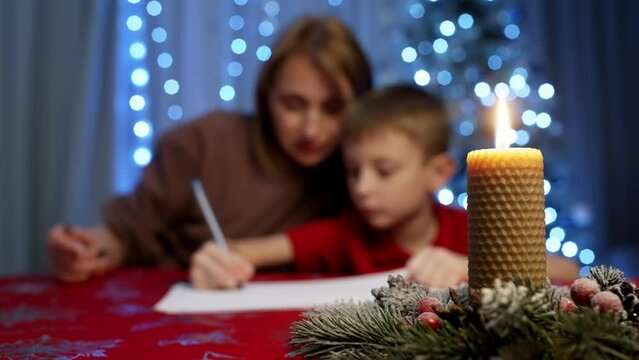 A mother helps her son write a letter to Santa Claus. Happy childhood, children's dreams beat the Christmas tree. High quality 4k footage