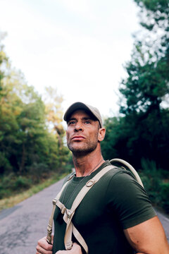 Army man in uniform with backpack and cap standing on road against trees in forest