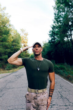 Confident special force commando on road saluting with pride against forest