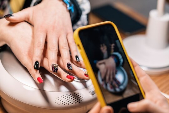 Crop manicurist taking picture of nail art on client in salon