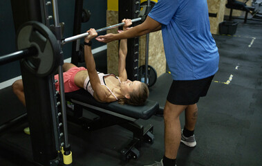 Personal trainer assisting gym-goer with bench press