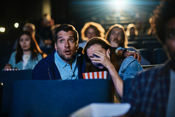 Scared young couple watching scary movie at theater