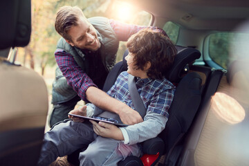 Father fastening son seatbelt for road trip