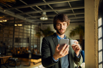 Young man drinking coffee using smartphone in modern office