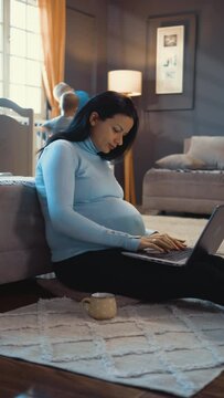 Vertical shot of a pregnant mother working on a laptop from home while her children play in the background