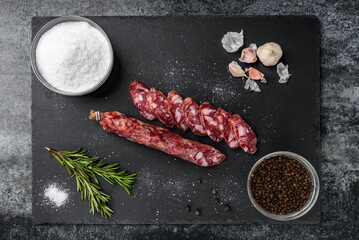 Smoked sausage salami and spices on black background.