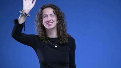 Cheerful Young Woman Waving Hello on Blue Background, Friendly Female in Her 20s Saying Hello to the Viewer