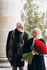 Obraz premium Elderly couple, handsome old man gives a huge bouquet of red flowers to his lady on a valentines day