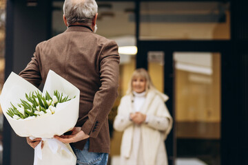 Elderly couple together, man waiting with a bouquet of tulips for his lady