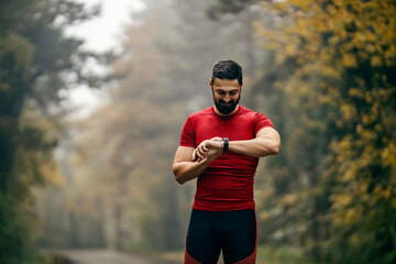 A fit sportsman is using smart watch fitness app on rainy and foggy weather in nature.