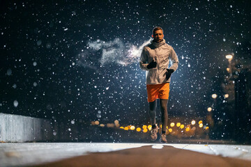 An urban sportsman is running at night on snowy weather.