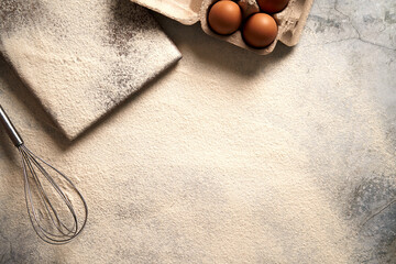 Baking background with flour, eggs and egg whisk. Horizontal photo.