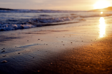 A low sea wave rolls off the beach at sunset. A sunny path