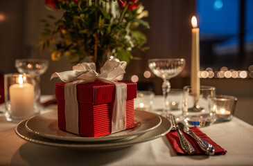holidays, dinner party and celebration concept - close up of festive table serving with gift box, flowers in vase and candles burning at home on valentine's day