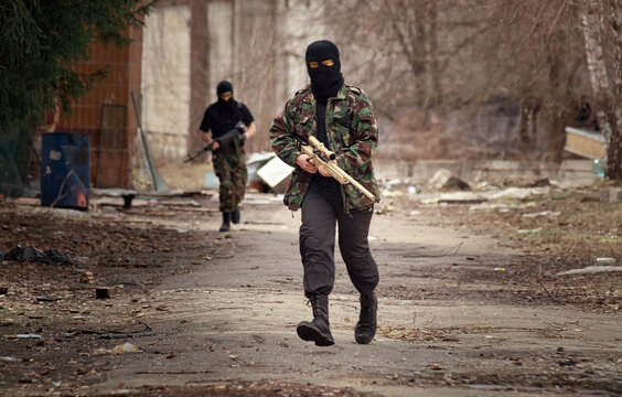 Soldier or terrorist man wearing balaklava mask running with sniper rifle in his hand on city battlefield