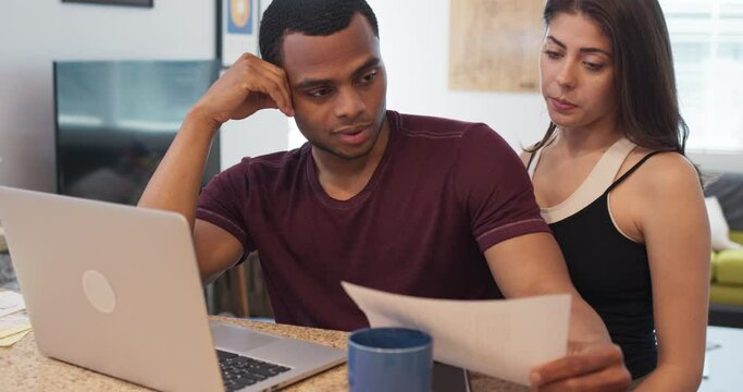 Millennial couple sitting at kitchen counter looking over unexpected bills. Young newlywed homeowners planning budget over breakfast. Man and woman with student loans. 4k slow motion handheld