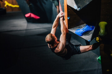 Young athletic guy in black tank top climbing climbing wall at climbing competition