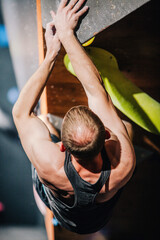 Young athletic guy in black tank top climbing climbing wall at climbing competition