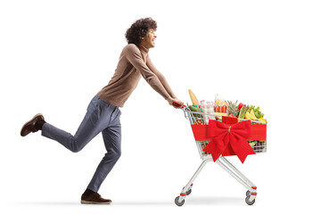 Full length profile shot of a young man running with a christmas shopping cart