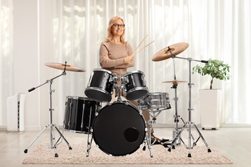 Mature female drummer posing with a drum set - obrazy, fototapety, plakaty
