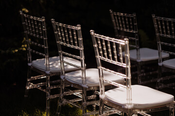 Row of elegant, transparent chairs with white cushions set outdoors in soft sunlight. Concept:...