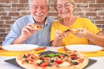 Happy senior couple ready to bite a slice of pizza. Elderly woman and man share a traditional Italian pizza for dinner