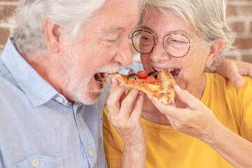 Close up portrait of senior caucasian couple having fun together eating a pizza. Elderly woman and...