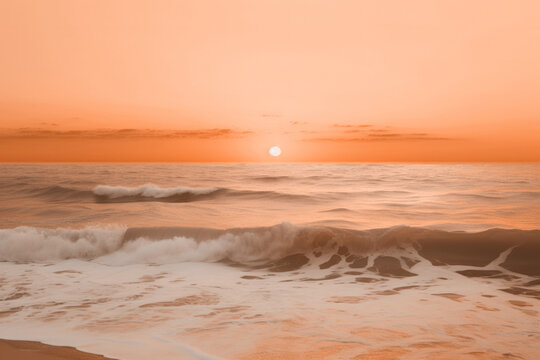 A serene beach at sunset with gentle waves under a soft peach fuzz color sky. Modern trendy tone hue shade