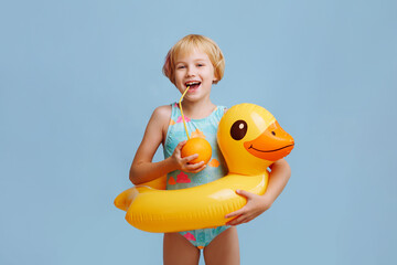 A child in a blue-orange swimsuit with an inflatable duck ring on a blue background. Drinks orange...