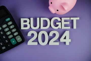 Budget 2024 alphabet letters with piggy bank and calculator top view on purple background