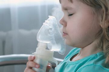 A little girl, a child of European appearance, wearing an inhaler mask. Treatment of seasonal diseases with a nebulizer at home. - obrazy, fototapety, plakaty