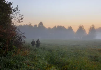 Foto op Plexiglas Two men with guns go in search of hunting object at sunrise. © okyela
