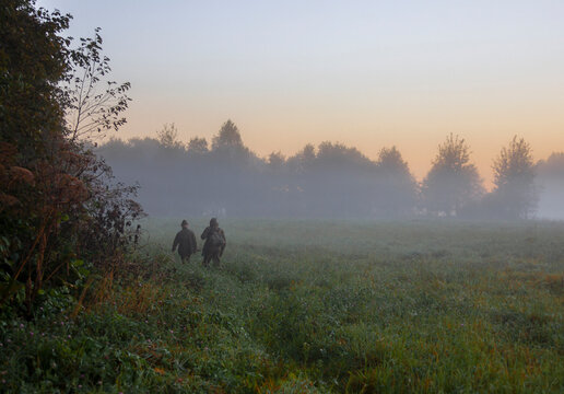 Two men with guns go in search of hunting object at sunrise.