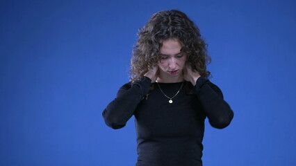 Stressed young woman rubbing neck trying to appease mental anguish while standing on blue background