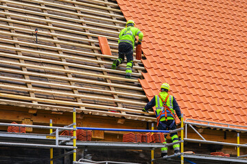 Two roofers in protective workwear installing new clay tiles, new clay tiles layer covering